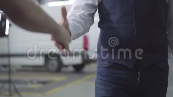 两名白种人男子在汽车修理厂握手男性手在背景的车辆汽车业务视频的预览图