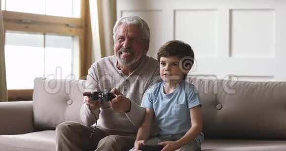 情绪化的老爷爷和小孙子拿着操纵杆玩电子游戏视频的预览图