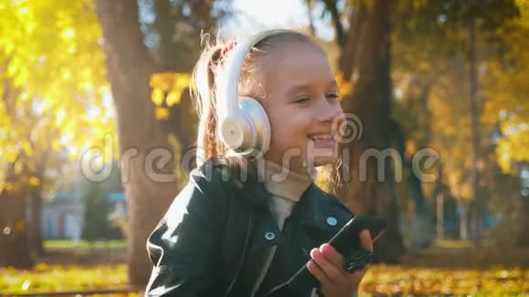 年轻女孩戴着耳机听音乐在秋天的城市公园里唱最喜欢的歌女孩是个了不起的人视频的预览图