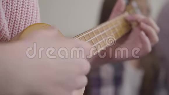 极端近距离的女性白种人的手玩四弦琴穿着粉色毛衣在室内练习的年轻天才女孩视频的预览图