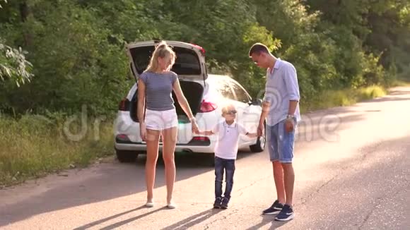 一个小孩子牵着父母的手在靠近汽车的路上跳得很高视频的预览图