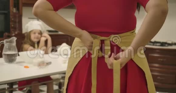 穿红色裙子系围裙的白人女人的后景一个模糊的小女孩坐在桌子的背景和视频的预览图