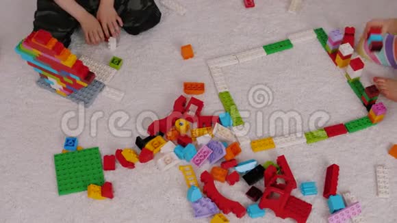 孩子们在幼儿园里坐在地毯上玩彩色塑料构造器视频的预览图
