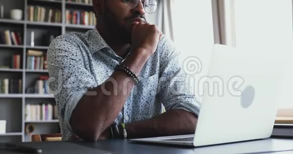 严肃体贴的美国商人坐在办公桌前看笔记本电脑视频的预览图