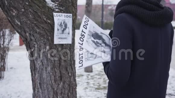 背面看着不可辨认的女人穿着蓝色冬衣站在失踪的宠物广告和签名前面一名女子视频的预览图