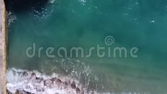 翡翠波冲刷着一个有混凝土桥墩和大卵石的海滩俯视图视频的预览图