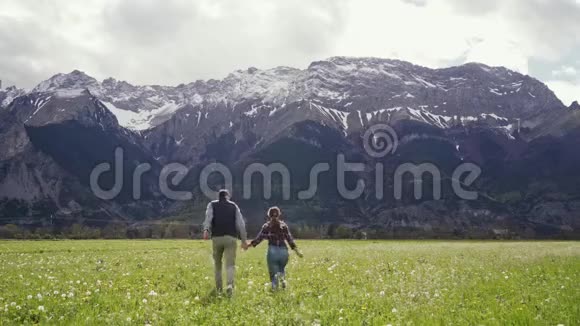 回头看情侣相爱出走手牵手在蒲公英的田野上与风景雪山春天一般视频的预览图