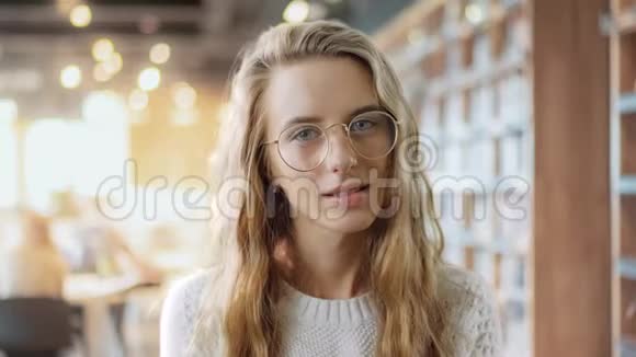 一个戴眼镜的聪明女孩在大学图书馆的背景下看着摄像机的照片聪明的少年视频的预览图