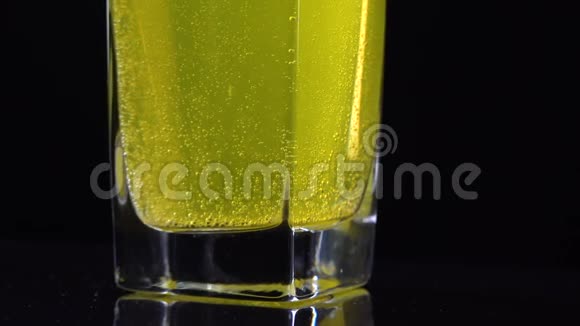 在黑暗的背景下将溶解在一杯新鲜矿泉水中的维生素C片剂封闭起来黄色起泡的大镜头视频的预览图