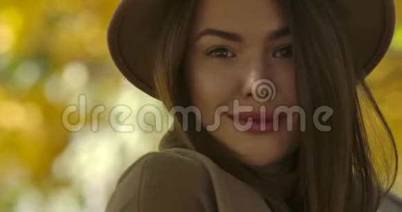 一位年轻迷人的欧洲女性戴着棕色帽子在黄叶背景下对着镜头摆姿势优雅优雅视频的预览图