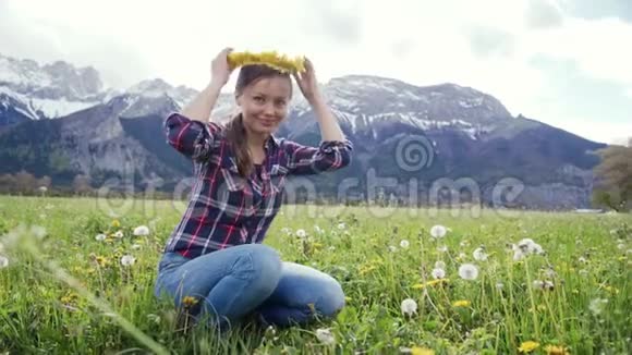 在风景秀丽的山景背景上身着格子衬衫的微笑女子在身上戴上蒲公英花环视频的预览图