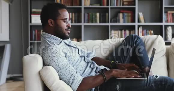 在家里沙发上用笔记本电脑放松严肃的非洲男人视频的预览图