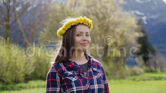美丽微笑的黑发女孩头上戴着蒲公英花圈在山上的花田上肖像视频的预览图