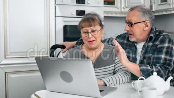 在舒适的厨房里用笔记本电脑拥抱一对老夫妇视频的预览图