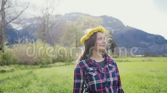 一个美丽的女孩用蒲公英花环的浪漫肖像美丽的女孩站在群山的背景上视频的预览图