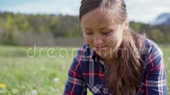 美丽的年轻女子穿着格子衬衫编织着一个草甸蒲公英花的花环微笑女孩的肖像视频的预览图