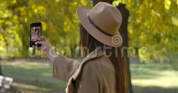 回到高加索年轻女孩棕色帽子和外套自拍智能手机令人愉悦的欧洲女性消费视频的预览图