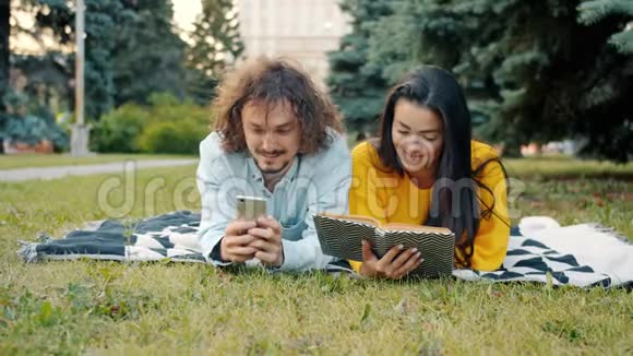 男人和女人用智能手机和看书聊天放松公园视频的预览图