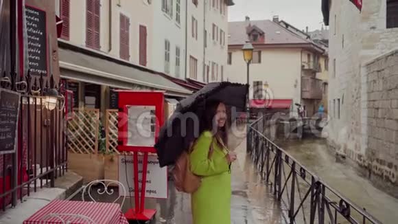 穿着黄色外套的女人在雨天的欧洲老街上带着黑色圆点伞走着视频的预览图