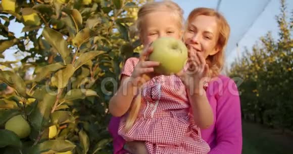 微笑的孩子正在展示一个绿色的大苹果而母亲抱着她4K视频的预览图