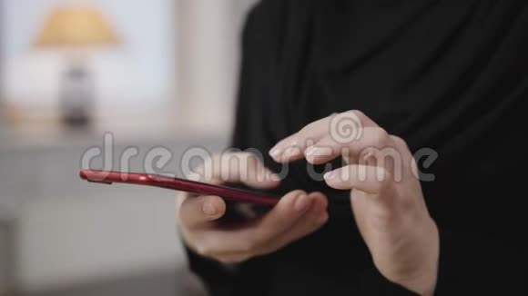 在智能手机上滚动的女性手的特写穿黑色衣服的年轻穆斯林妇女使用手机现代社会视频的预览图