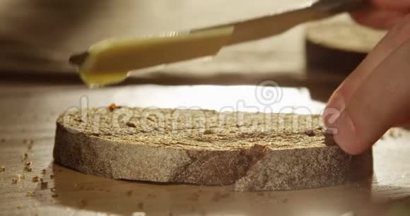 将黄油涂在带有阳光和太阳花的木桌上用一把手工编织的面包片上视频的预览图