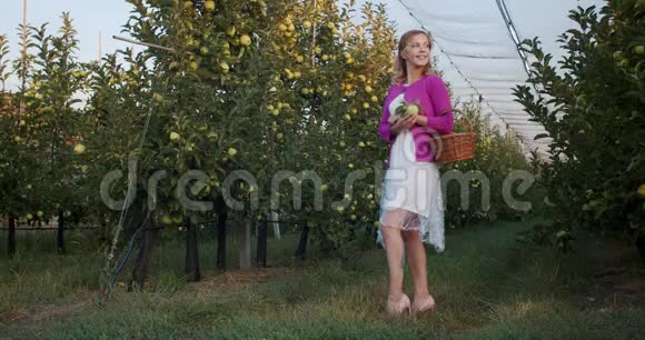 一位身穿白色礼服的金发女郎正在苹果园摆姿势微笑着4K视频的预览图