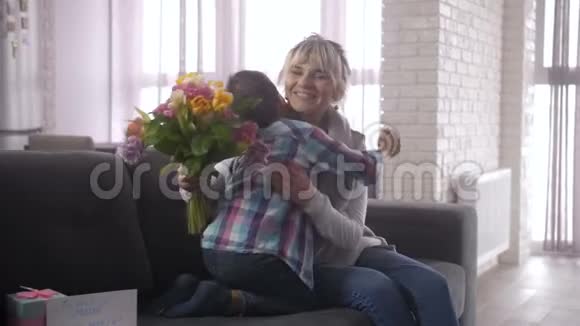 在母亲节快乐的妈妈在沙发上拥抱可爱儿子视频的预览图
