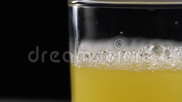 鲜榨的菠萝汁倒在桌上的玻璃杯里黑色背景上清爽的黄色饮料视频的预览图