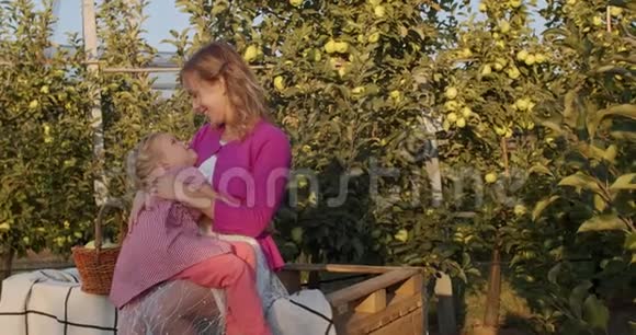 年轻的母亲抱着女儿坐在苹果园里4K视频的预览图