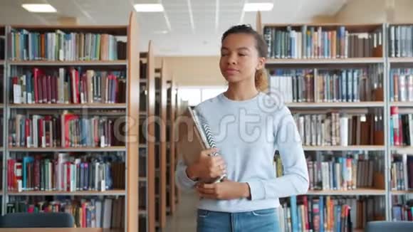 美国黑人女孩在大学图书馆散步手里拿着书四处张望视频的预览图