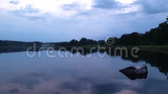 在平静的夏夜欣赏绚丽的日落湖岸有绿树和植物在晶莹洁净的镜面水中倒影视频的预览图