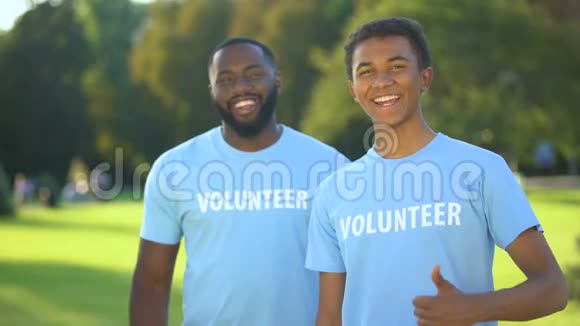 两个快乐的美国男人穿着志愿者T恤衫竖起大拇指无私地帮助视频的预览图