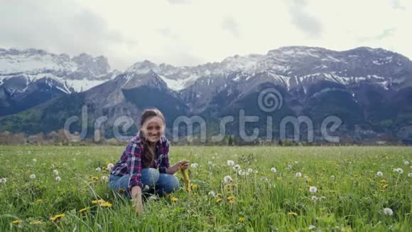 快乐的女孩编织着一个黄色的蒲公英花圈坐在山上的草地上斯拉夫民族视频的预览图