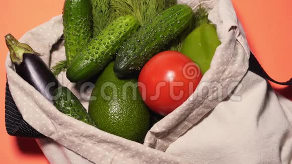 一个男人把蔬菜放在一个独立的彩色背景上的棉袋里黄瓜西红柿鳄梨等视频的预览图