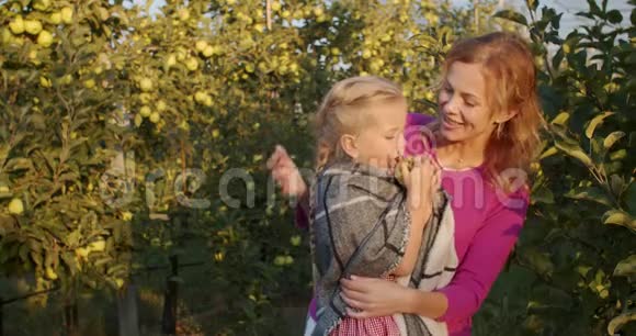 年轻的母亲抱着女儿她吃了一个苹果果园4k视频的预览图