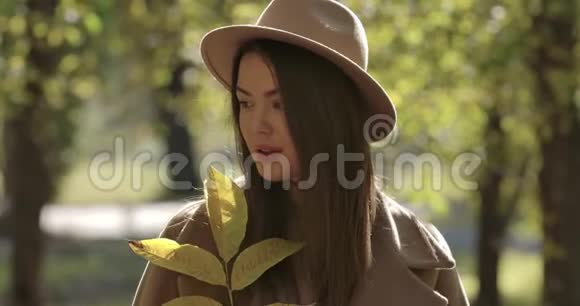 秋天公园里戴棕色帽子的可爱高加索女孩看着相机微笑的肖像漂亮的欧洲女人视频的预览图