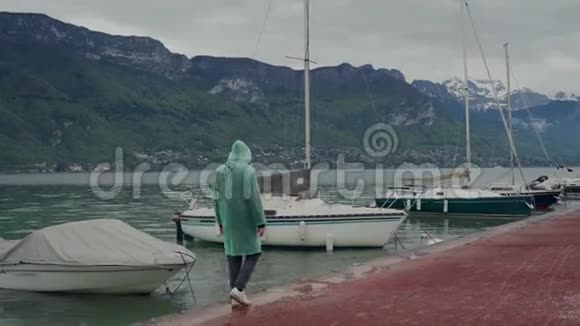 在雾蒙蒙的天气里一个穿着浅绿色雨衣的人在停泊在湖面上的帆船附近行走白天鹅游泳视频的预览图