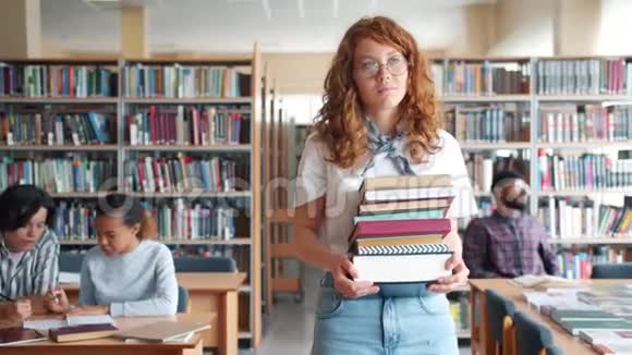 一位严肃的红头发女士在图书馆里走来走去手里拿着一堆书视频的预览图