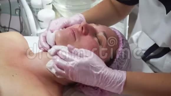 美容师在美容室用湿巾清洁成年女性的面部视频的预览图