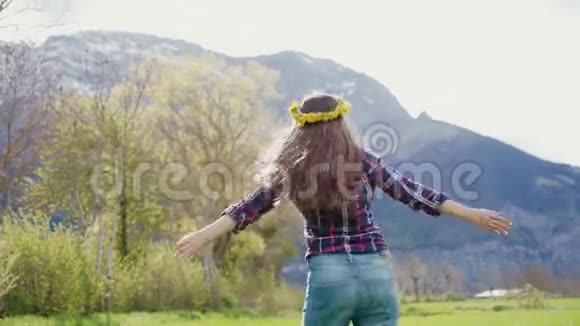 美丽的女人带着蒲公英的花环微笑着转过身来双臂伸到山上的风景上视频的预览图