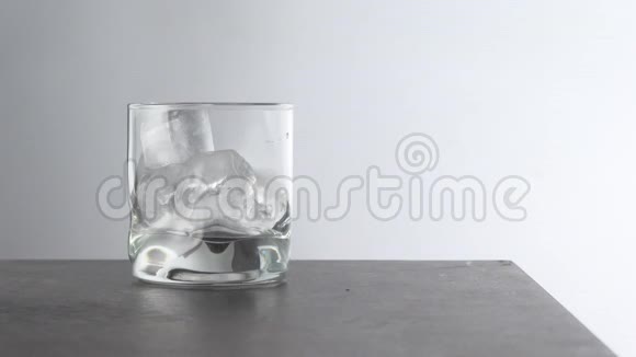 酒保把陈年的金色威士忌倒入一个杯子里桌子上放着冰块带有白色岩石的琥珀色酒精饮料视频的预览图