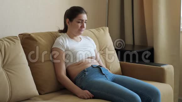 年轻的女人坐在沙发上伤心胃的重量过多视频的预览图