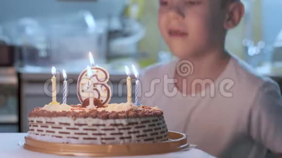 小男孩坐在厨房的桌子旁旁边放着点着蜡烛的生日蛋糕视频的预览图