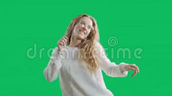 戴着耳机的快乐年轻女子正在用智能手机听音乐在绿色屏幕背景下跳舞和微笑视频的预览图