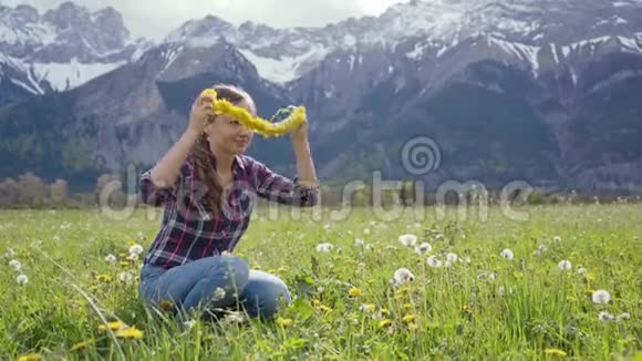 合上美丽的年轻女子编织着一个草地蒲公英花圈在群山的背景上试着自己视频的预览图