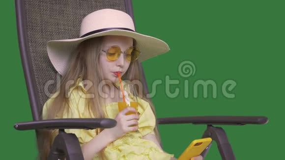 夏天喝橙汁和看智能手机的年轻女孩女孩坐在椅子上享受水果鸡尾酒视频的预览图