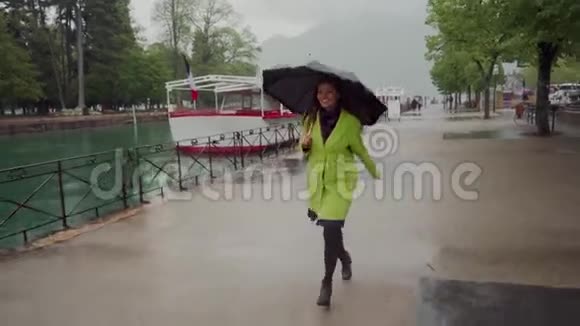 快乐的女人穿着黄色的外套带着黑色的圆点伞沿着白色游艇的长廊在雨中奔跑视频的预览图