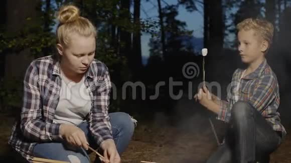 在森林徒步旅行中孩子们在篝火上用木棍准备棉花糖女孩和男孩青少年吃棉花糖视频的预览图