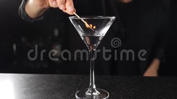 女调酒师用燃烧的棍子在酒精鸡尾酒上缓慢地点燃酒精饮料着火视频的预览图